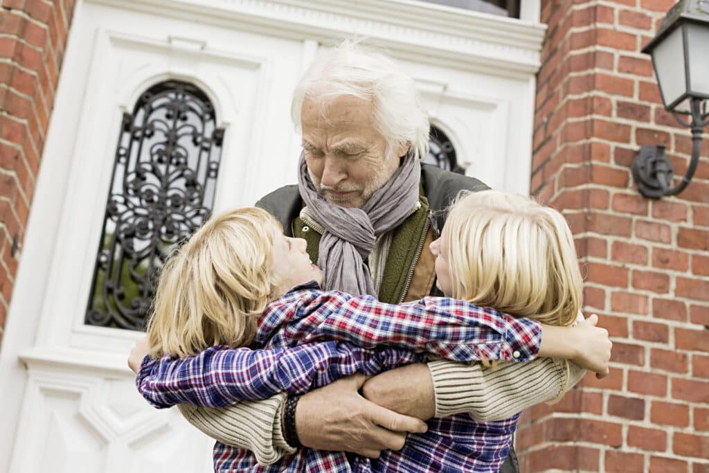 Grandfather hugging grandchildren by front door